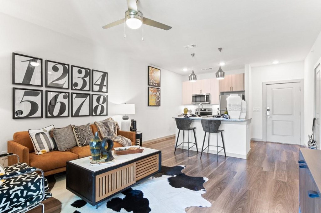 A living room with a brown sofa and a coffee table with a black and white patterned ottoman.