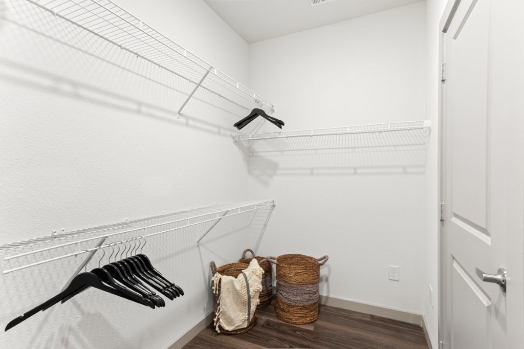 A white closet with clothes hanging and baskets on the floor.