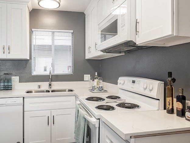 A white kitchen with a stove, sink, and cabinets.
