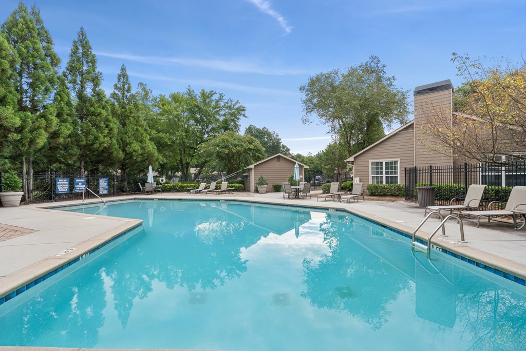 A large swimming pool surrounded by trees and chairs.