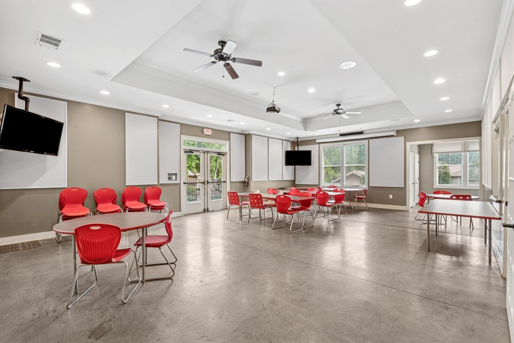 A room with a white ceiling and a fan, and a table with red chairs.