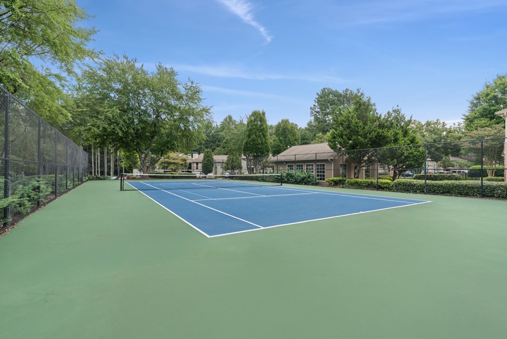 A tennis court surrounded by trees and a fence.