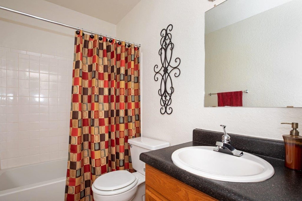 A bathroom with a white toilet, a black counter top, and a shower curtain with a pattern of squares and rectangles.