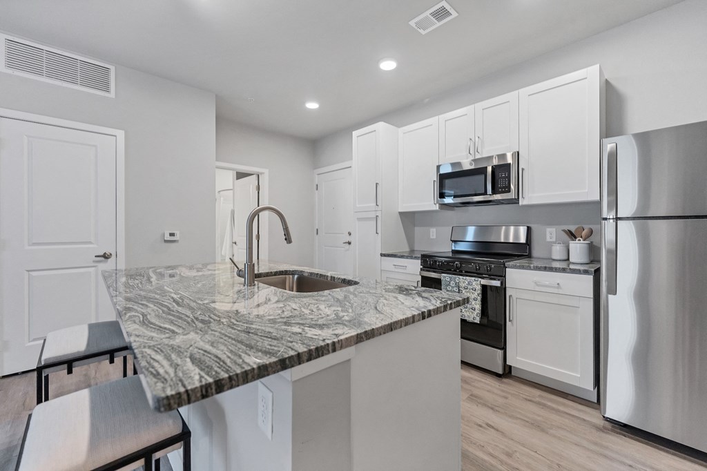 an open kitchen with white cabinets and a marble counter top
