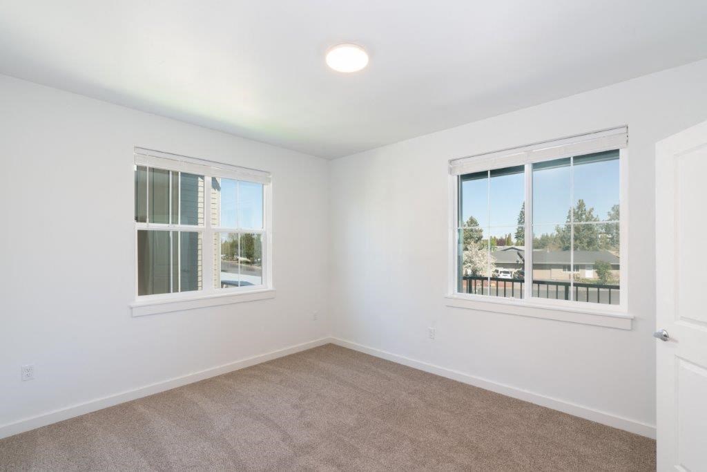 an empty bedroom with two windows and a door to a balcony
