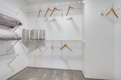 a walk in closet with a white wall and a rack with hangers