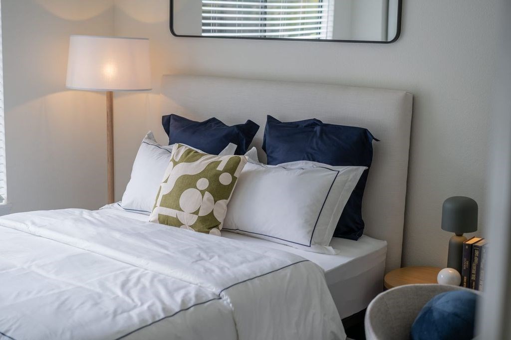 A bed with white sheets and blue and green pillows.