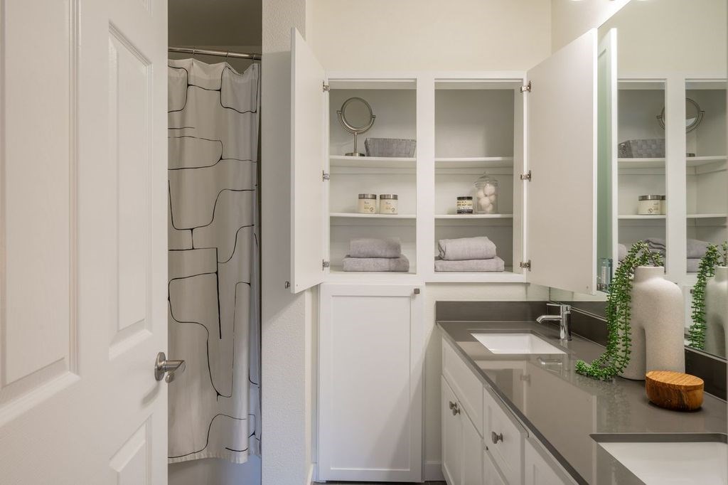A bathroom with a white shower curtain and a white cabinet with a mirror above it.