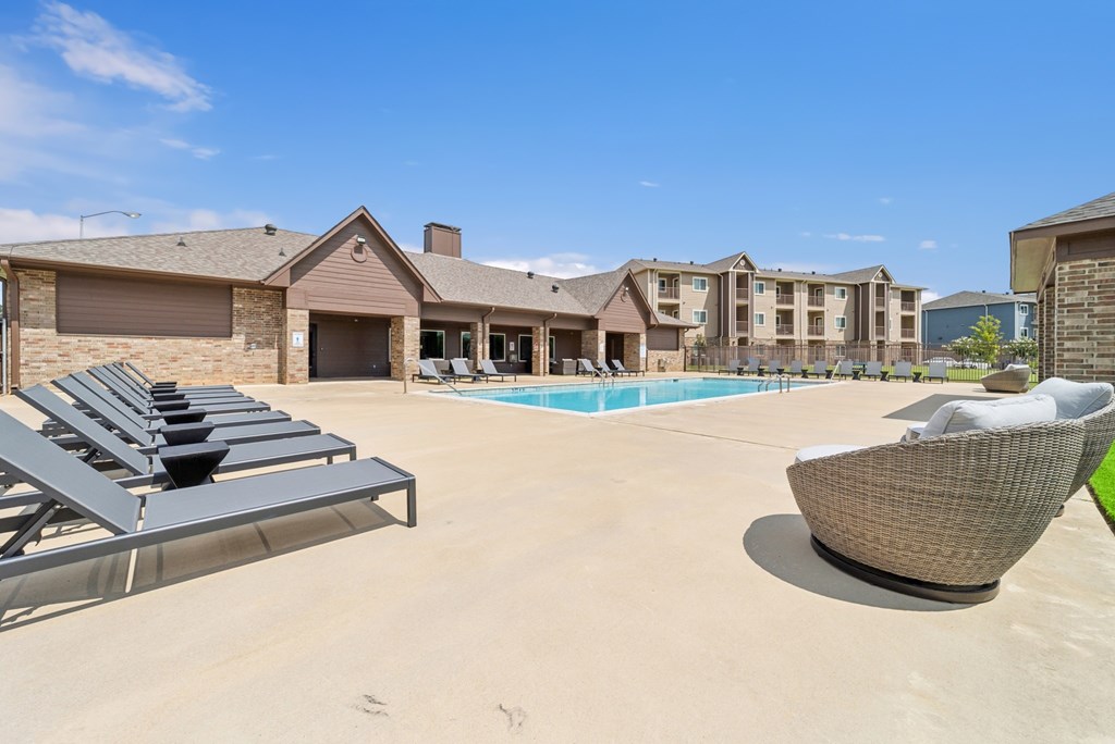 A sunny day at the poolside with lounge chairs and a building in the background.