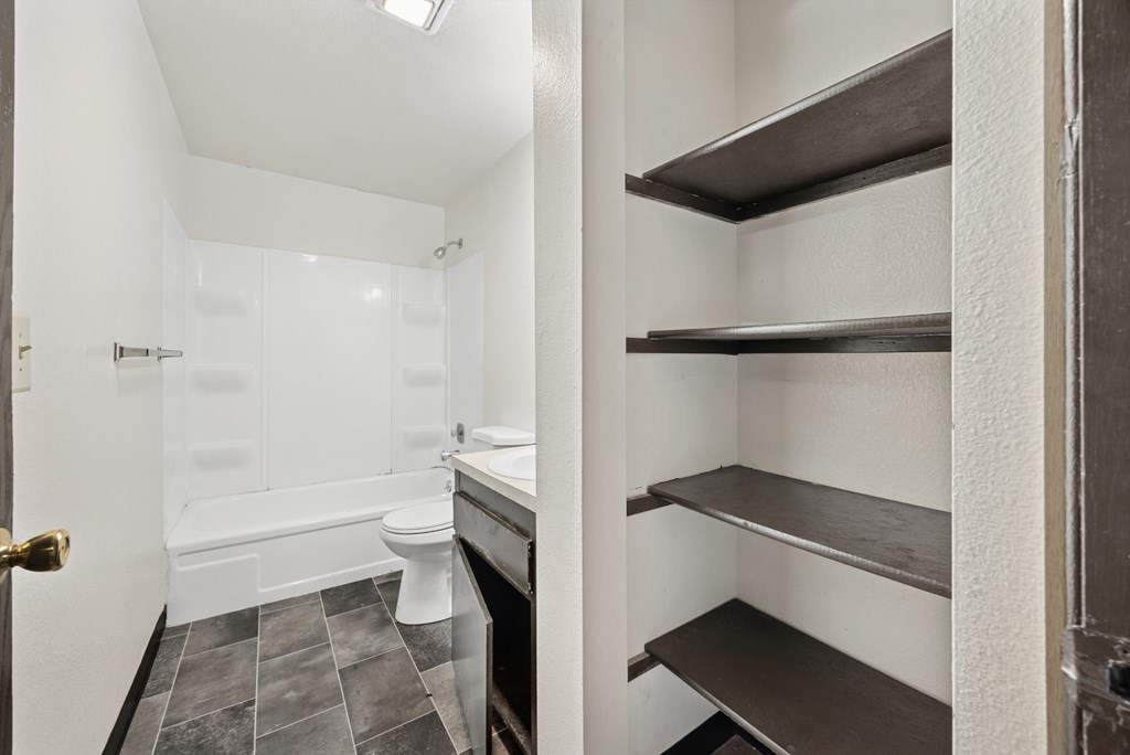 A white bathroom with a toilet, sink, and shelves.