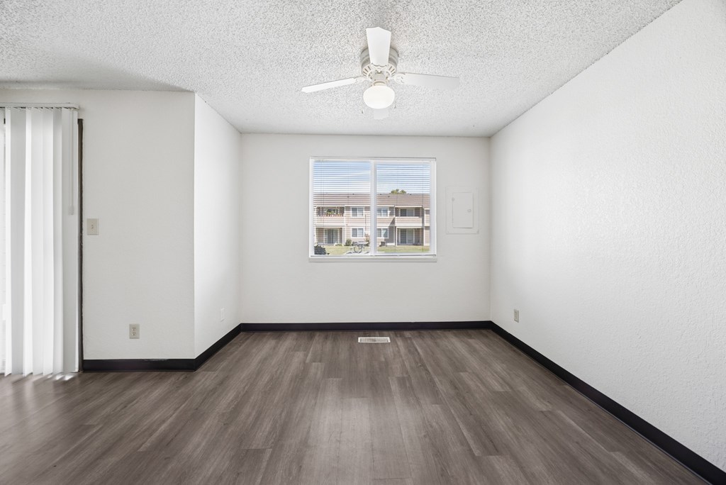 A room with a ceiling fan and a window showing a building outside.