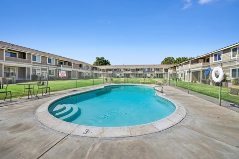 A round swimming pool in the middle of a concrete area with buildings in the background.