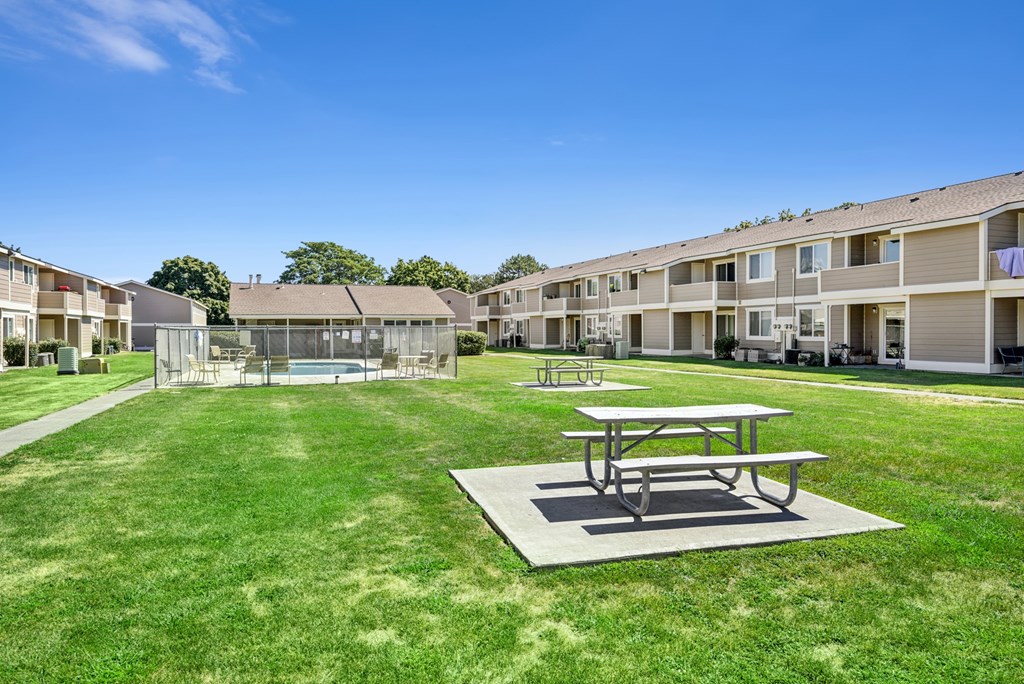 A picnic table sits in the middle of a grassy area in front of apartment buildings.