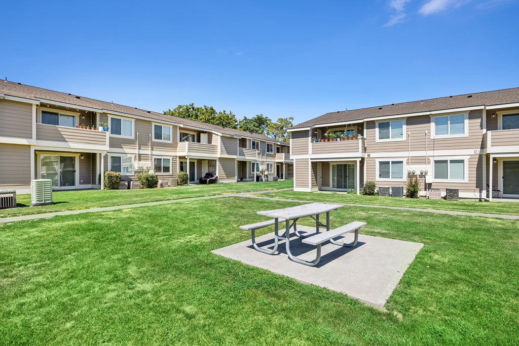 A large grassy area with a picnic table in the middle of apartment buildings.