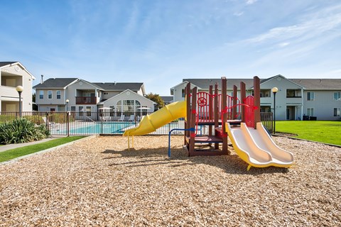 A playground with a yellow slide and red structure.