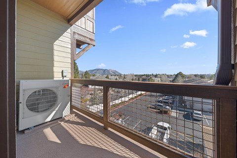 A balcony with a fan and a view of a parking lot and mountains.