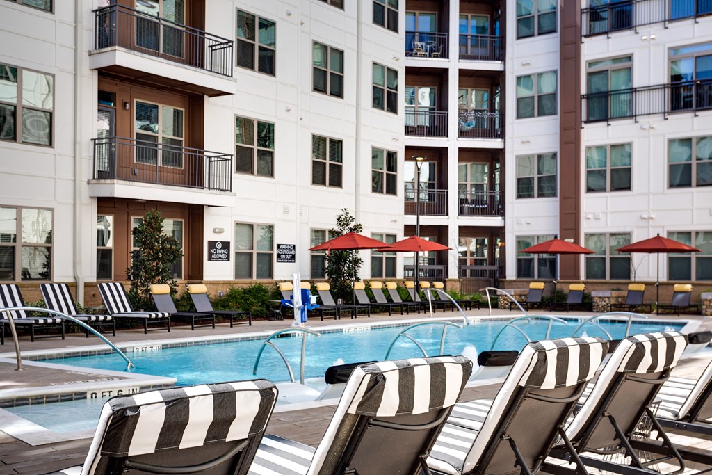 a swimming pool with lounge chairs and umbrellas in front of a building
