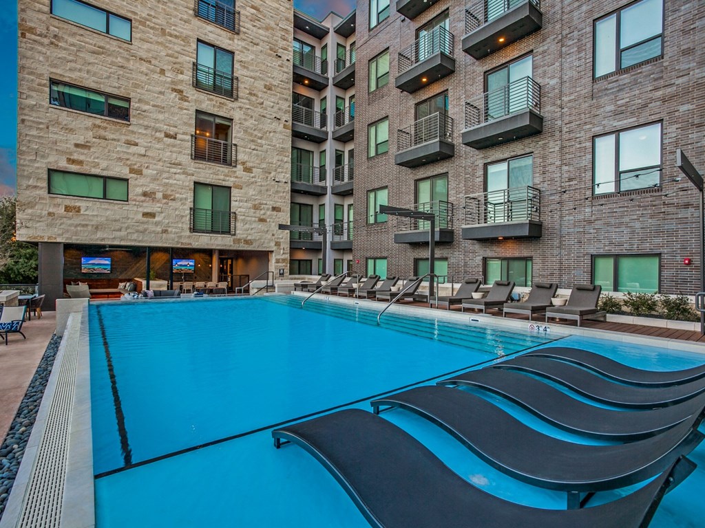 a swimming pool with chaise lounge chairs in front of an apartment building
