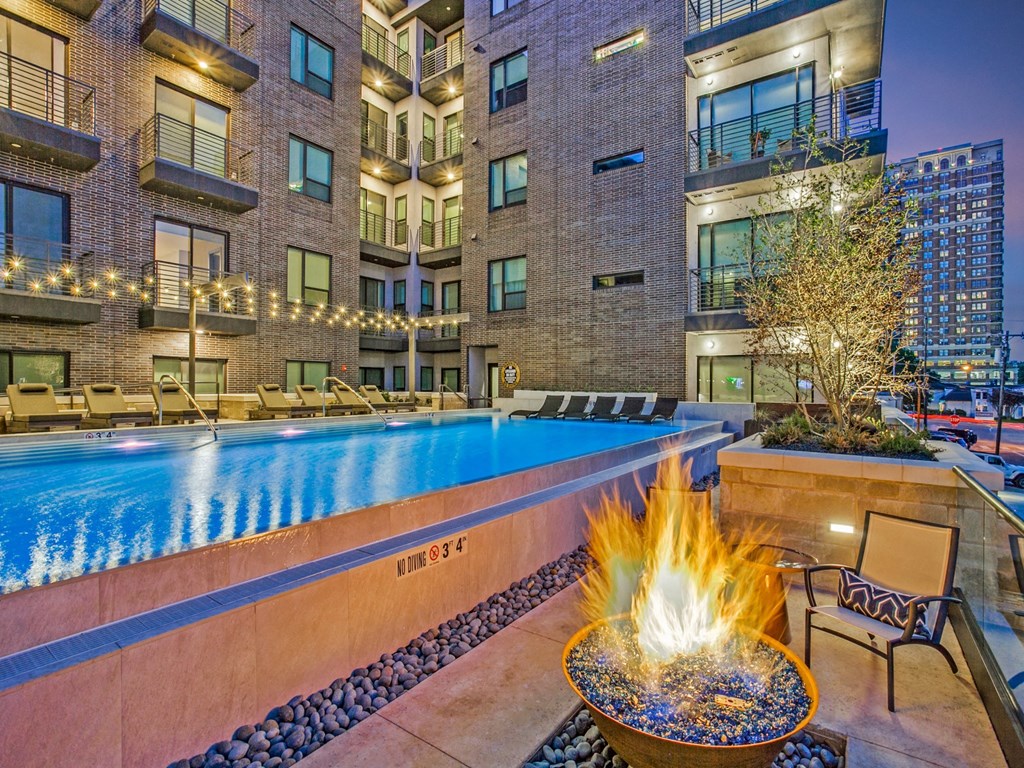 a pool with a fire pit and lounge chairs in front of an apartment building