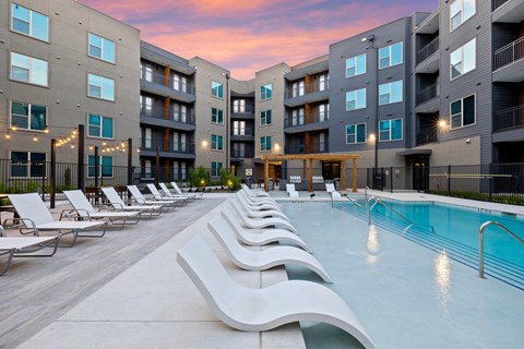 A swimming pool surrounded by lounge chairs in front of apartment buildings.