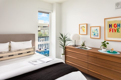 A bedroom with a bed, nightstand, and a window overlooking a cityscape.