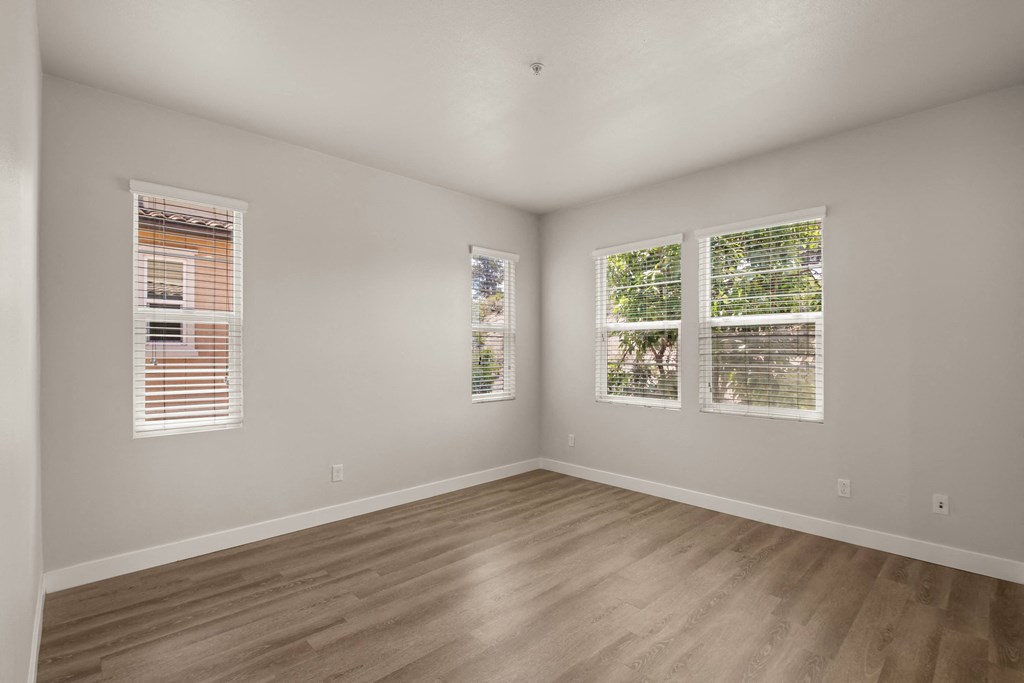 an empty room with wood floors and three windows
