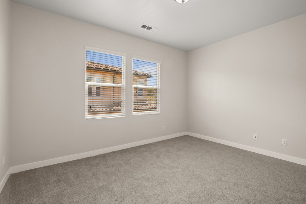 an empty room with two windows and carpeting