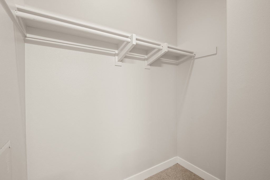 a spacious closet in a bedroom with white walls and a white rack on the ceiling