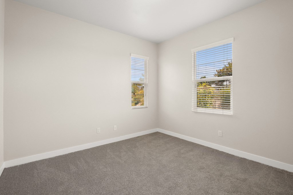 an empty room with carpet and two windows