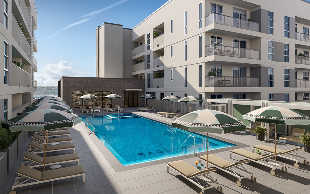 A swimming pool surrounded by sun loungers and umbrellas in front of apartment buildings.