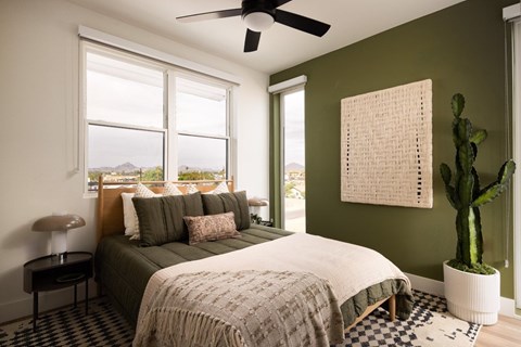 A bedroom with a bed, a cactus, and a fan.