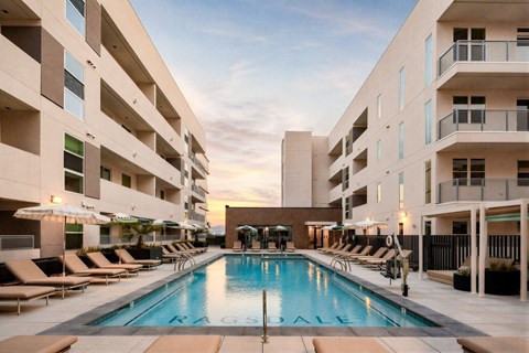 A large swimming pool in the middle of a courtyard surrounded by lounge chairs and umbrellas.