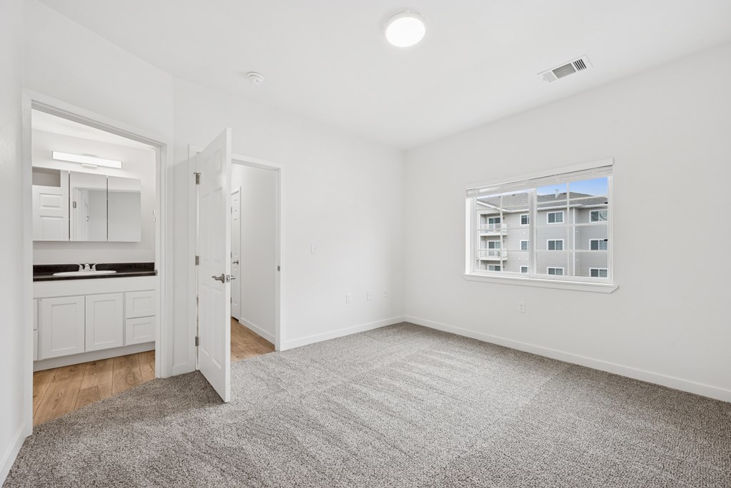 A spacious room with a grey carpet and a window showing a building outside.
