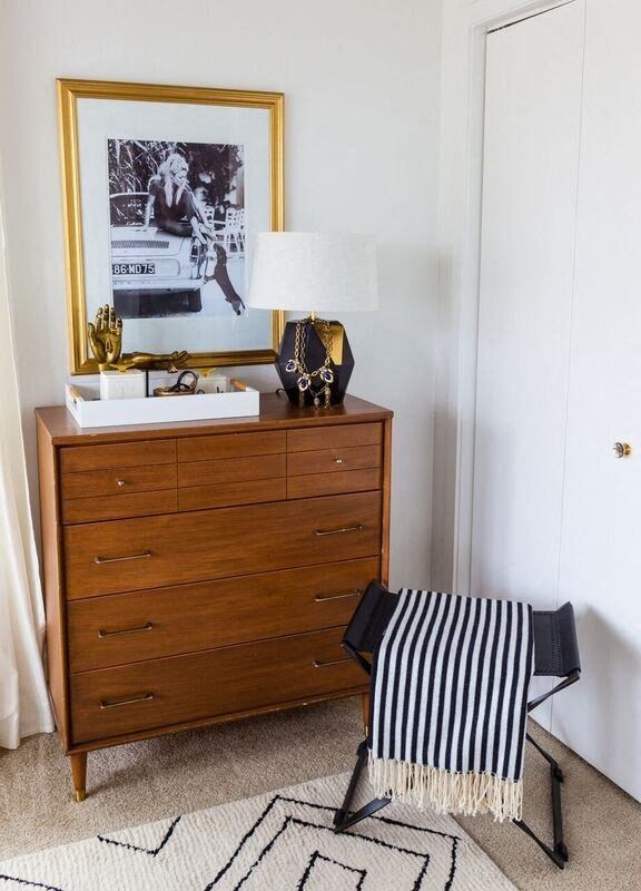 a dresser with a lamp and a striped stool on top of it