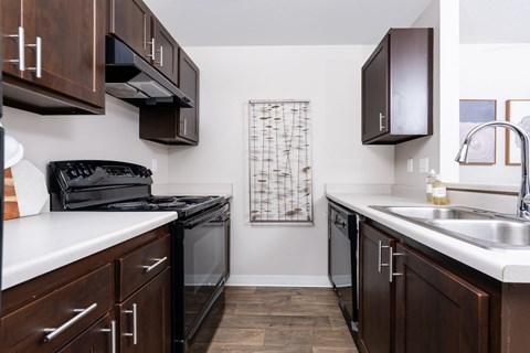 a kitchen with dark wood cabinets and white counter tops and a black stove and sink