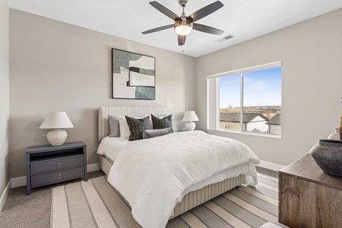 A bedroom with a large bed, a ceiling fan, and a view of the outdoors through a window.