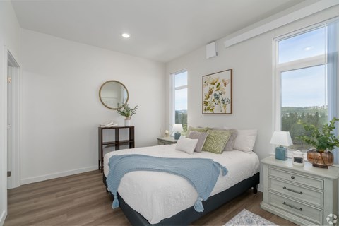 A bedroom with a bed, nightstand, and a round mirror on the wall.