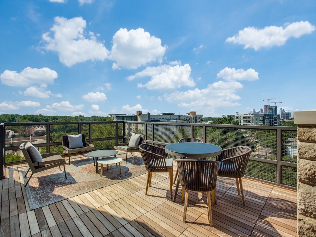 a patio with a round table and chairs on a wooden deck with a view of the city