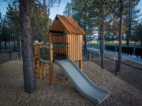 A playground with a wooden structure and a grey slide.