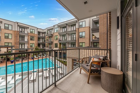A balcony with a pool and chairs in front of apartment buildings.