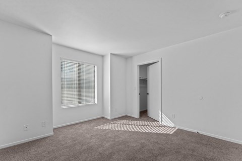 a bedroom with white walls and carpet and a door to a closet