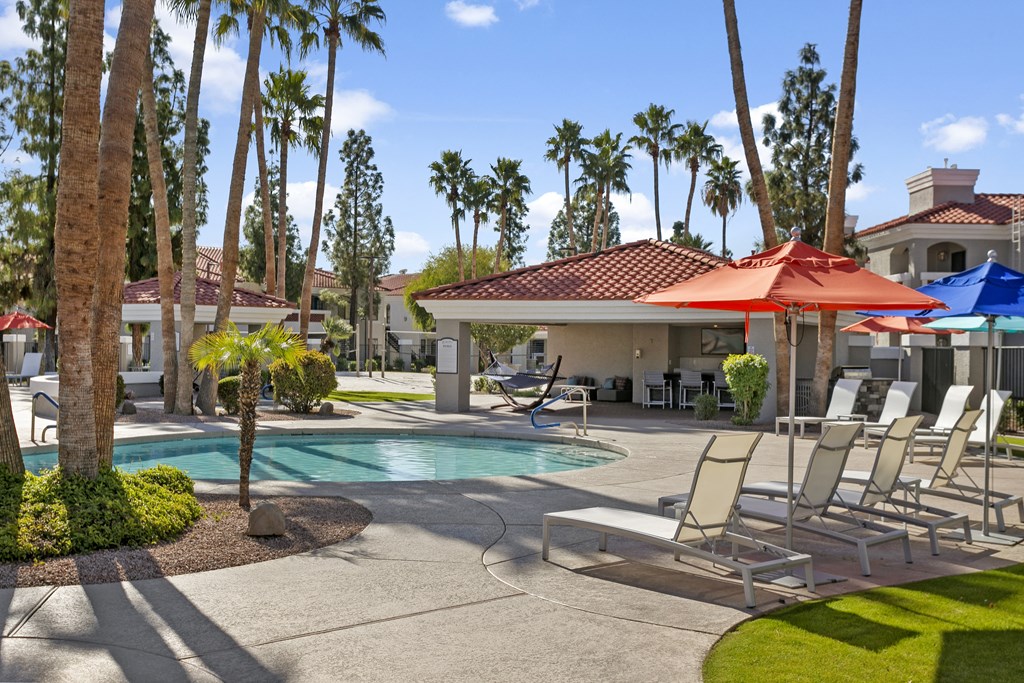 a swimming pool with chairs and umbrellas in front of a house