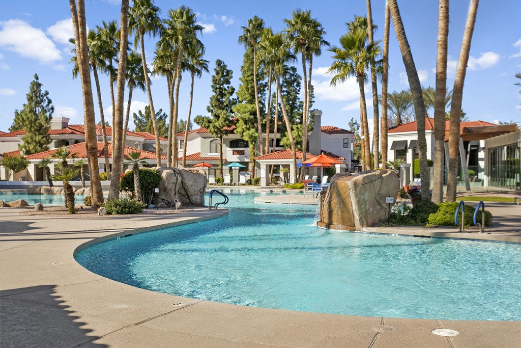 a large swimming pool with a waterfall and palm trees