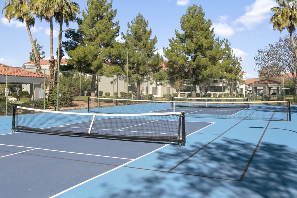 two tennis courts with trees and buildings in the background