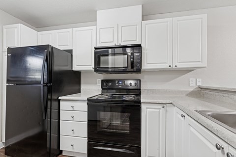 A black refrigerator and oven in a kitchen with white cabinets.
