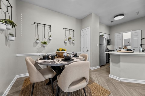 A dining room with a table set for two and a kitchen area in the background.
