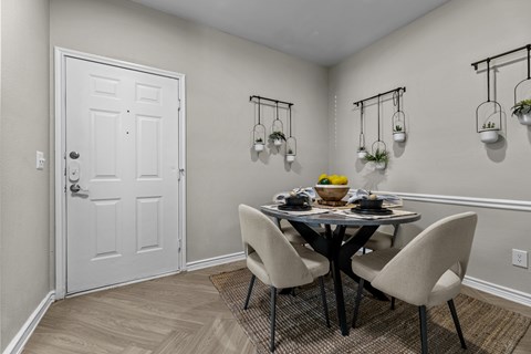 A dining room with a white door, a round table with four chairs, and three hanging planters.