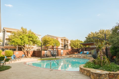 A swimming pool surrounded by a stone wall and trees.