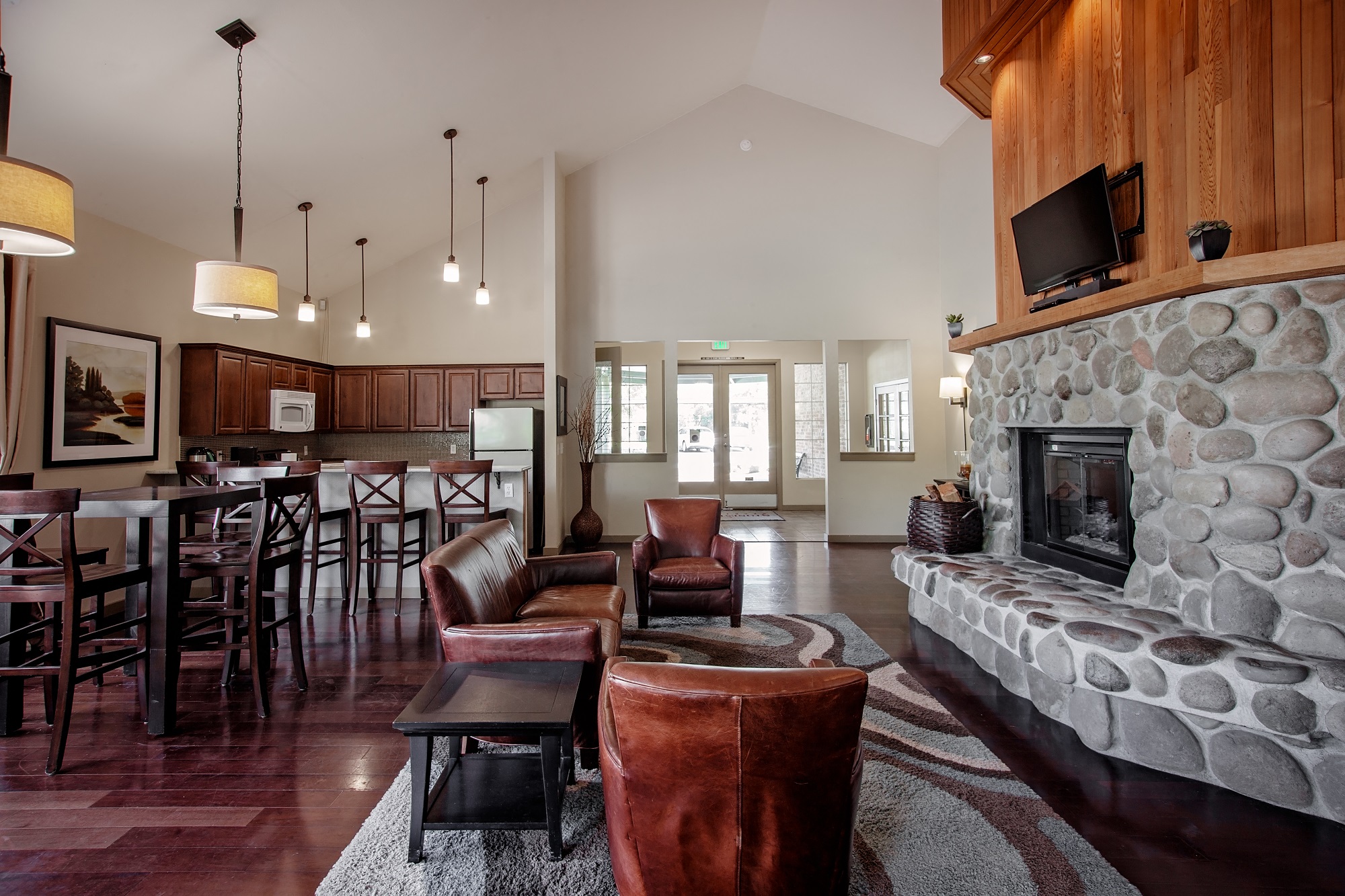 A living room with a stone fireplace and a dining table with chairs.