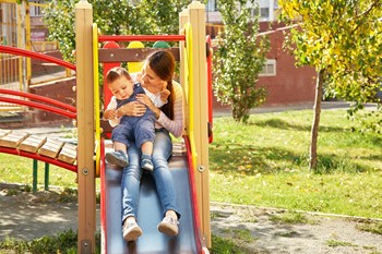 Mother and Child Going Down Slide at Playground Together Smiling - Photo Gallery 3
